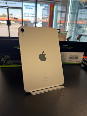 An Apple iPod Touch in a light gold finish, showing the back of the device with the Apple logo and 'ipod' text, resting on a dark surface with store windows in the background.