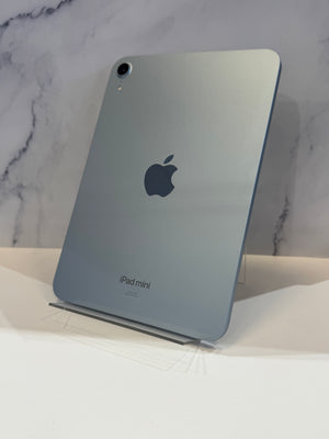 A silver Apple iPad mini standing upright on a clear display stand against a white marble-patterned background.