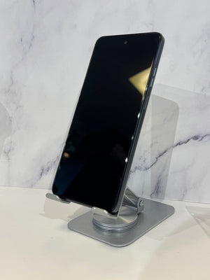 A black smartphone displayed upright on a silver metal stand against a white marble-patterned background.