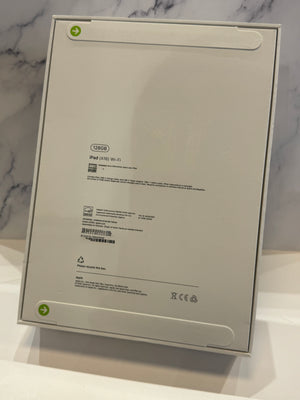 The back of a white IKEA iPad box, showing product specifications and barcodes, standing on a white surface against a light gray marble-patterned background.