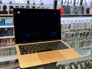 Gold laptop on a glass surface with shelves of phone cases in the background