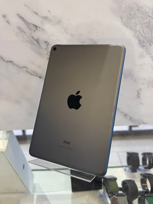 An Apple iPad with a metallic gray back, standing on a clear display stand in a retail setting against a white marble-patterned background.