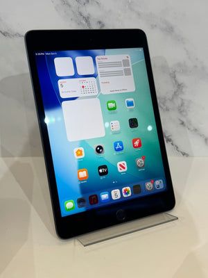 A black Apple iPad tablet standing upright on a clear acrylic display stand against a white marble-patterned background.