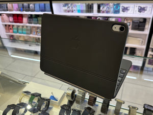 A black Apple iPad with a matching folio case and attached keyboard, displayed on a stand inside a retail store. The Apple logo is embossed on the back of the case.