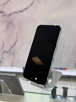 A black smartphone with a silver metallic edge, displayed on a clear acrylic stand on a glass counter against a white marble-patterned background.
