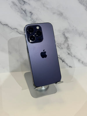 A dark blue-gray Apple iPhone 12 Pro Max standing upright on a small metallic display stand against a white marble-patterned background.