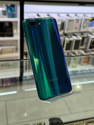 A holographic Honor smartphone with a green-to-blue iridescent finish, standing upright on a clear acrylic display stand inside a retail store.