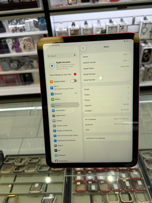 An Apple iPad with a red front bezel and black side edges, displaying the Settings app on its screen, photographed in a retail store environment with display cases in the background.