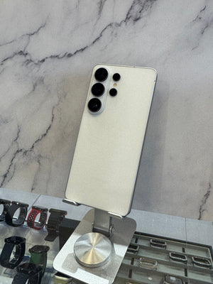 A silver Samsung Galaxy Ultra smartphone shown from the back, mounted on a metal display stand in a retail setting against a gray marble-patterned wall.