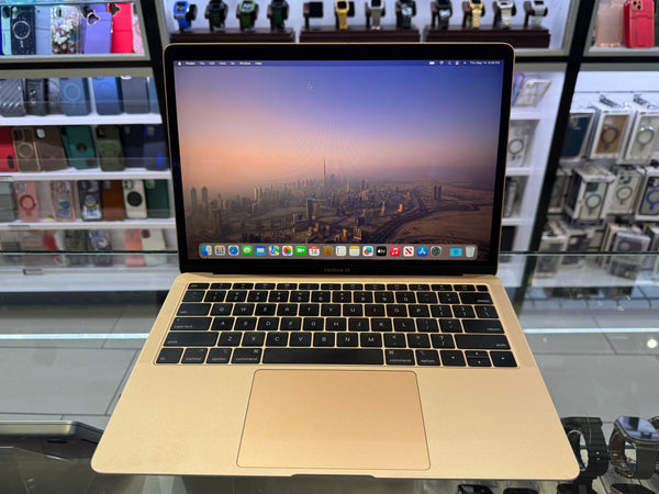 Apple laptop on a glass table with a cityscape on the screen, surrounded by electronic products.