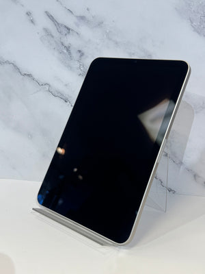 A black tablet with rounded corners and a silver edge, displayed upright on a clear acrylic stand against a white marble-patterned background.
