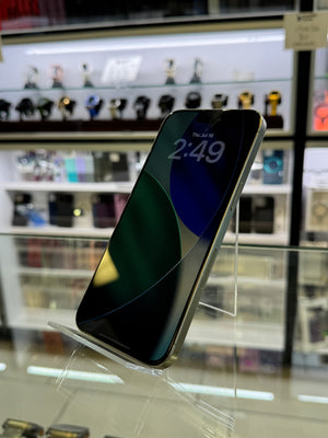 A black smartphone with a silver edge, displayed on a clear acrylic stand inside a retail store. The screen is on, showing the time 2:49 and a dark wallpaper.