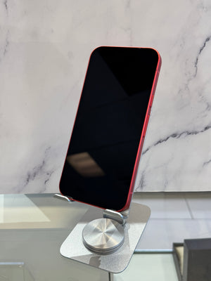 A red smartphone with a black screen stands upright on a silver metal display stand against a light marble-patterned background.