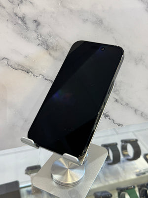 A black smartphone with a large front screen and silver side buttons, displayed on a metallic stand against a white marble-patterned background.