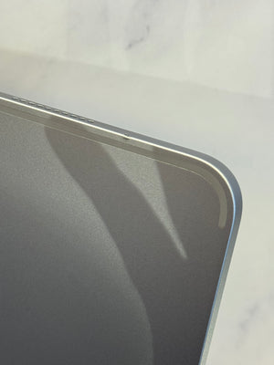 Close-up of the corner of a dark gray tablet or laptop showing a thin silver metallic edge against a light marble-like background.