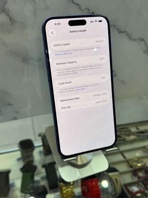 A black smartphone displaying the battery health settings screen, standing on a metallic display stand in a retail or showroom environment with a marble-patterned background.