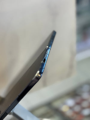 Close-up side view of a slim black smartphone showing the edge, button area, and camera cutout, photographed against a softly blurred indoor background.