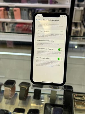 Smartphone displaying a battery health screen in a store setting with electronic devices in the background.