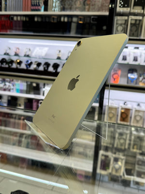 A silver Apple iPhone 7 displayed on a clear acrylic stand inside a retail store, with shelves of cameras and electronics blurred in the background.