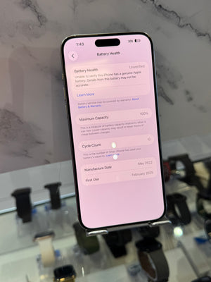 A black Apple iPhone displaying the battery health screen on its screen, resting on a display stand in a retail store environment.