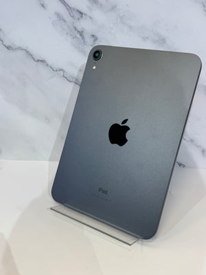 A gray Apple iPad shown from the back, standing upright on a clear acrylic display stand against a white marble-patterned background.