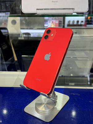 A red Apple iPhone with a silver Apple logo, displayed on a silver stand on a blue counter inside a store.