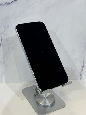 A silver aluminum magnetic phone stand holding a black smartphone, set against a white marble-patterned background.