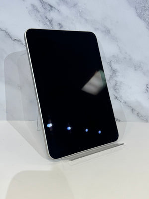A black tablet with rounded corners and a silver edge, displayed upright on a clear acrylic stand against a white marble-patterned background.