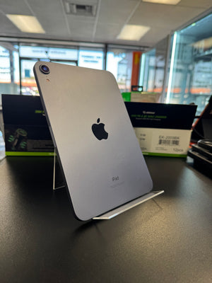 A silver Apple iPad shown from the back, standing on a clear display stand on a dark tabletop in a store or office setting.