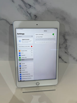 A white Apple iPad standing upright on a white surface against a light marble-patterned background, with the Settings app visible on the screen.