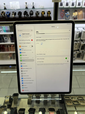 An iPad in a black case displayed on a clear stand inside a retail store, showing the battery settings screen on its screen.