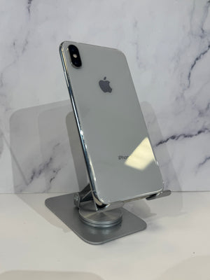 A silver Apple iPhone with a reflective glass back is displayed on a metallic gray stand against a white marble-patterned background.