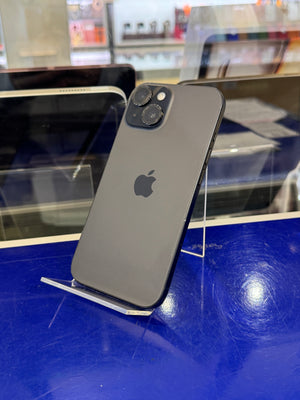 A dark gray Apple iPhone 12 Pro shown from the back, resting on a clear display stand against a blue counter in a retail setting.