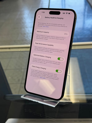 Smartphone displaying battery health and charging settings on a stand with a blurred background.