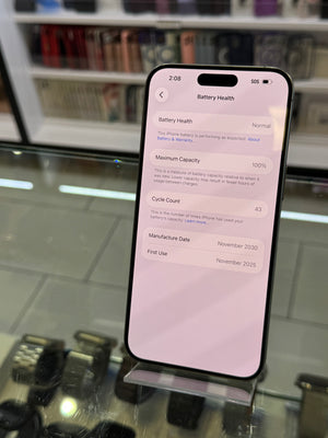 A black smartphone displayed on a stand in a retail setting, showing the battery health settings screen on its screen. The background shows blurred store shelves and display cases.