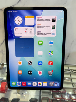 An iPad with a black bezel displaying its home screen, resting on a clear display stand in front of a marble-patterned background.