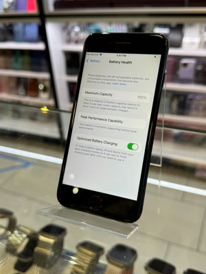Smartphone displaying battery health information on a glass surface with blurred shelves in the background