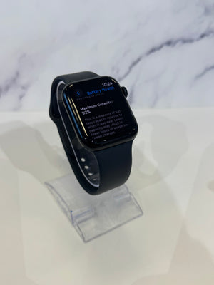 A black smartwatch with a black band displayed on a clear acrylic stand against a white marble-patterned background.