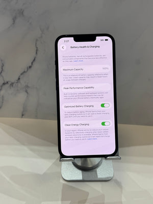 A smartphone displayed upright on a metal stand against a light marble-patterned background. The phone screen shows the iOS Battery Health & Charging settings page.