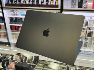 Black Apple laptop on display in a store with watches and jewelry in the background