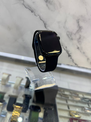 A black smartwatch with a glossy black screen and black band, displayed on a clear acrylic stand in a watch store with a marble-patterned background.