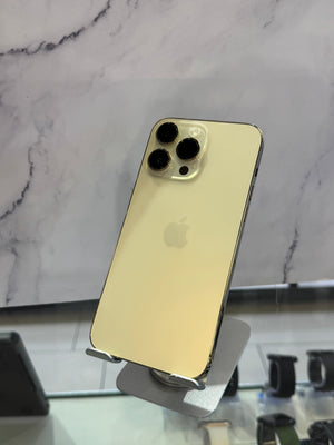 A gold-colored Apple iPhone Pro shown from the back, resting on a silver display stand against a white marble-patterned background.