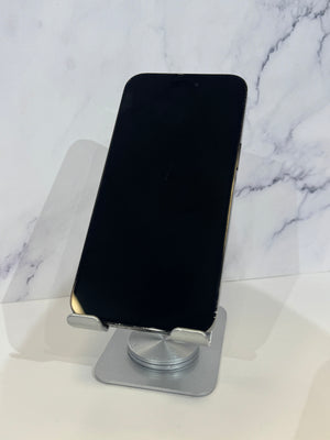 A black smartphone, resting vertically on a silver metal stand against a white marble-patterned background.