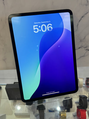 A tablet device with a black bezel and a blue-to-purple wallpaper, standing upright on a glass display counter in a retail setting.