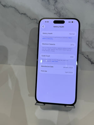 A black smartphone displayed upright on a small stand against a light marble-patterned background, showing the battery health settings screen on the display.