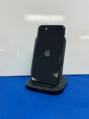 A black Apple iPhone standing upright on a dark gray charging dock against a white wall, with a blue surface underneath.
