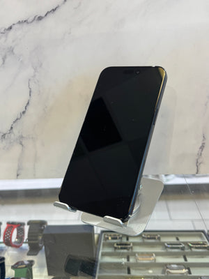 A black smartphone with a blank screen is displayed on a small metallic stand inside what appears to be a retail store, with a marble-patterned wall behind it and watch displays visible in the foreground.