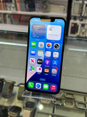 A black iPhone with a blue lock screen wallpaper displayed on a clear stand inside a retail store.