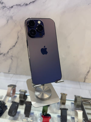 A dark blue-gray Apple iPhone shown from the back, mounted on a silver display stand on a white marble-patterned surface.