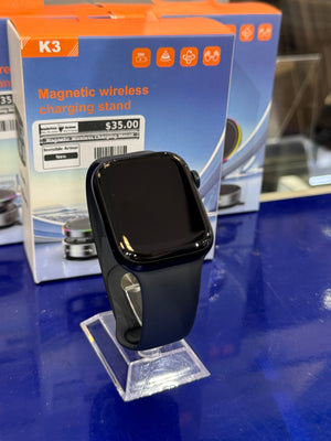 Black smartwatch on a clear stand with K3 magnetic wireless charging stand packaging in the background.